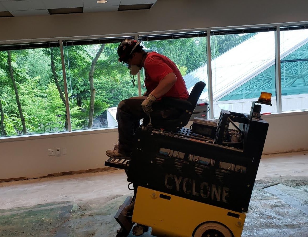 Ride-on floor scraper removing old flooring from a commercial concrete slab.
