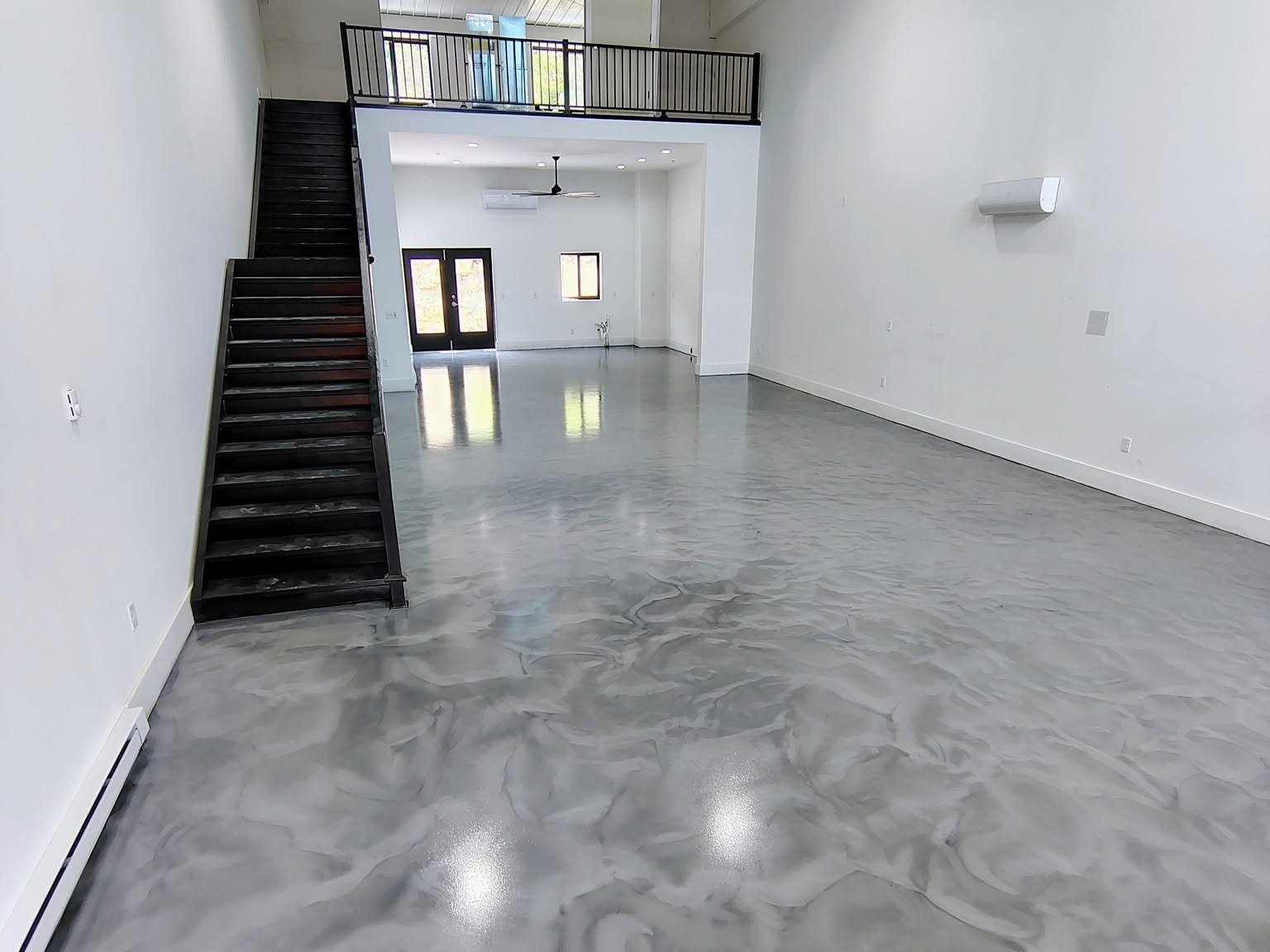 Gray and white metallic epoxy floor in an open room with a black staircase.