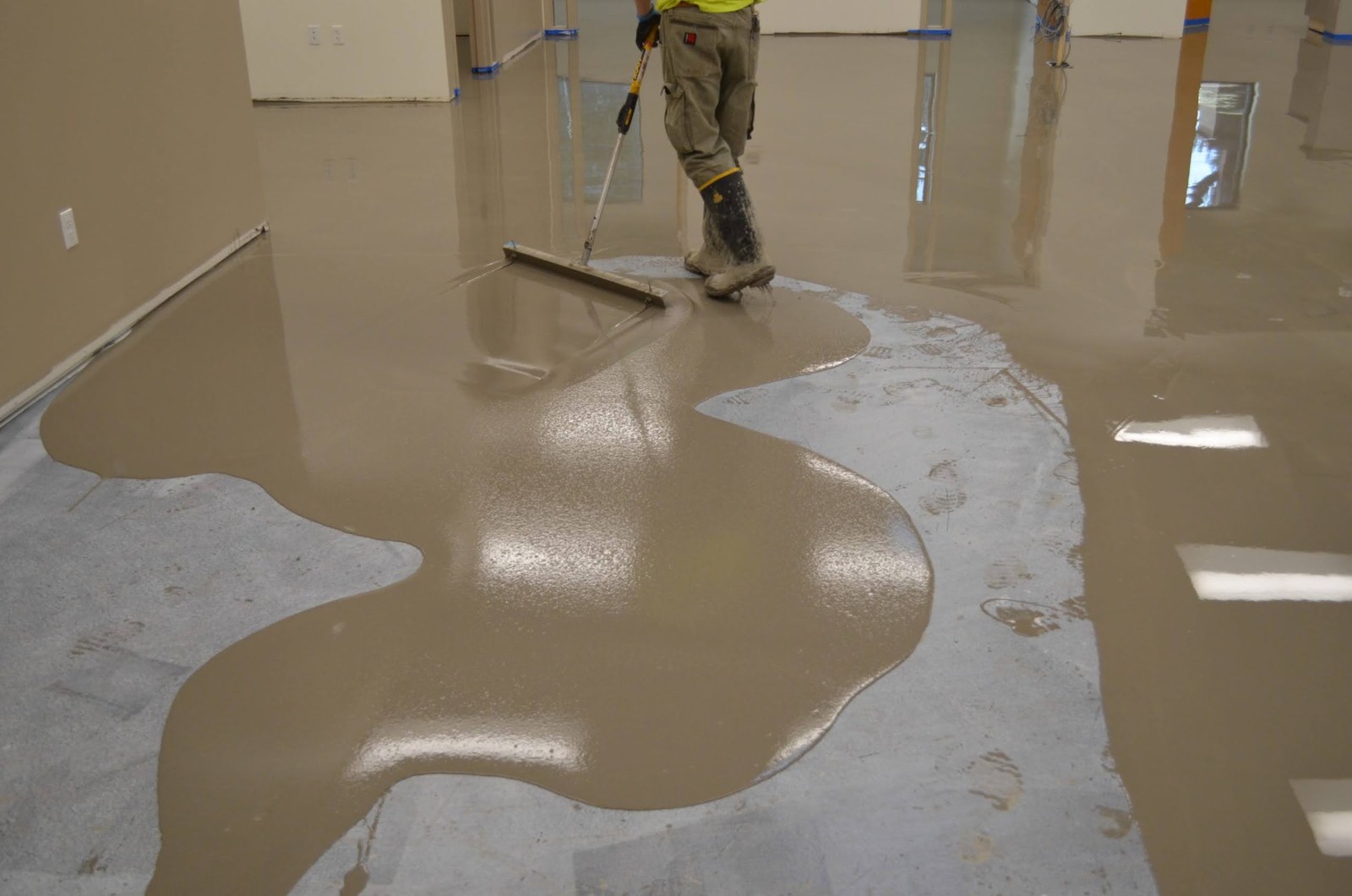 Self-leveling concrete being spread with a gauge rake over a commercial floor.